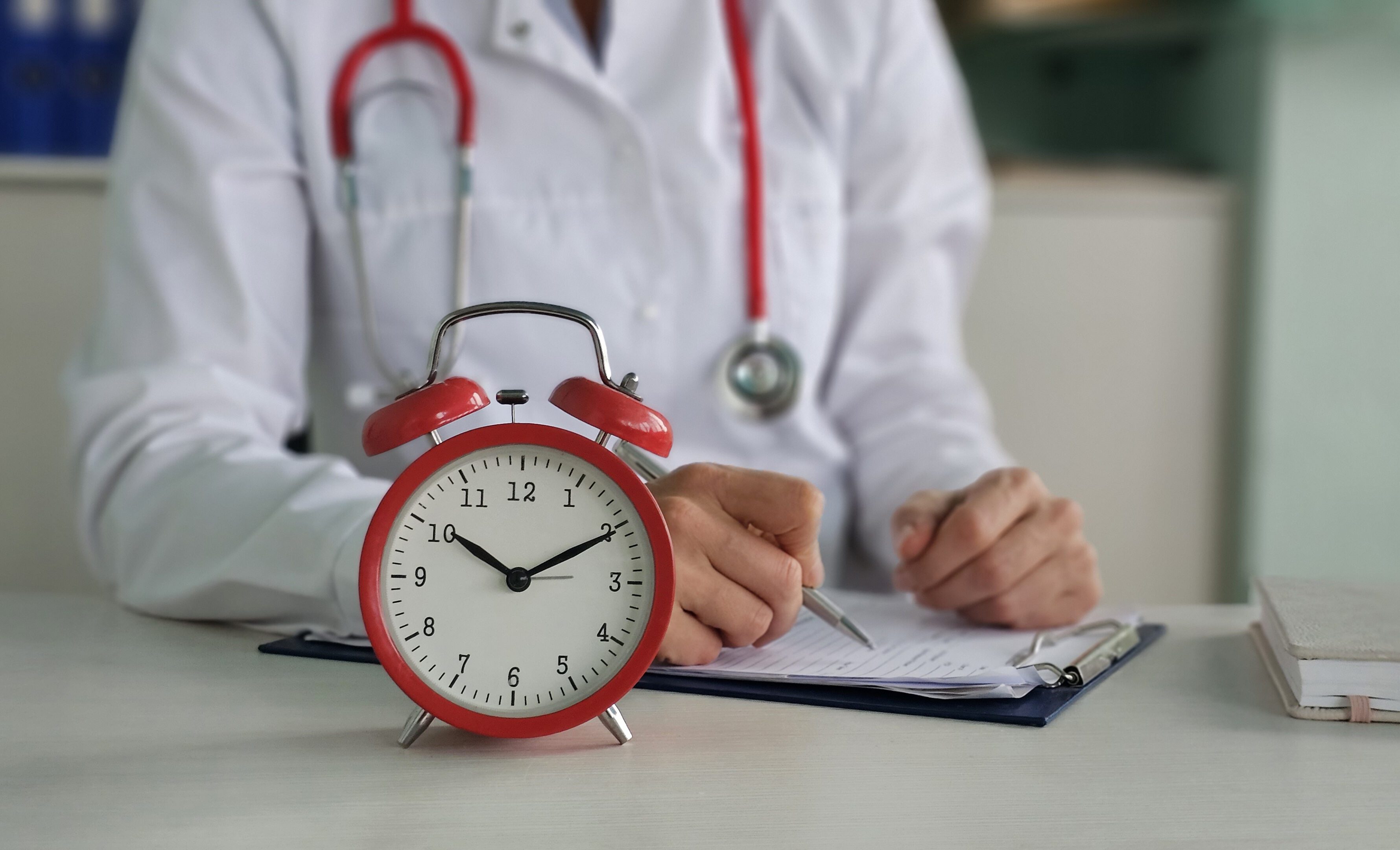 Red alarm clock on background of doctor in white coat. Medical insurance