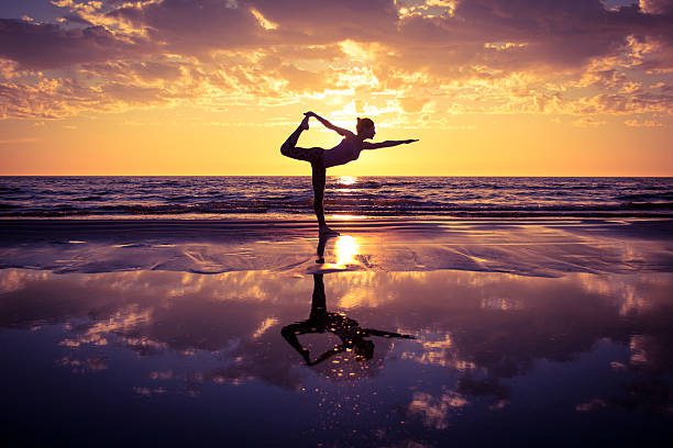 A person practicing yoga on the beach during sunset.